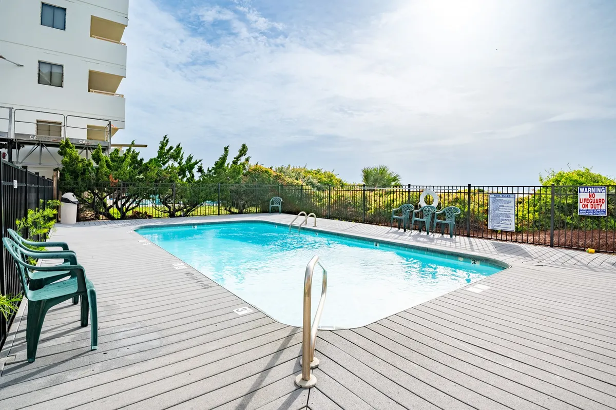 This image showcases a vibrant swimming pool surrounded by lounge chairs and a landscaped garden. The lifeguard sign hints at safety for families, while children can be imagined playing and adults relaxing poolside.