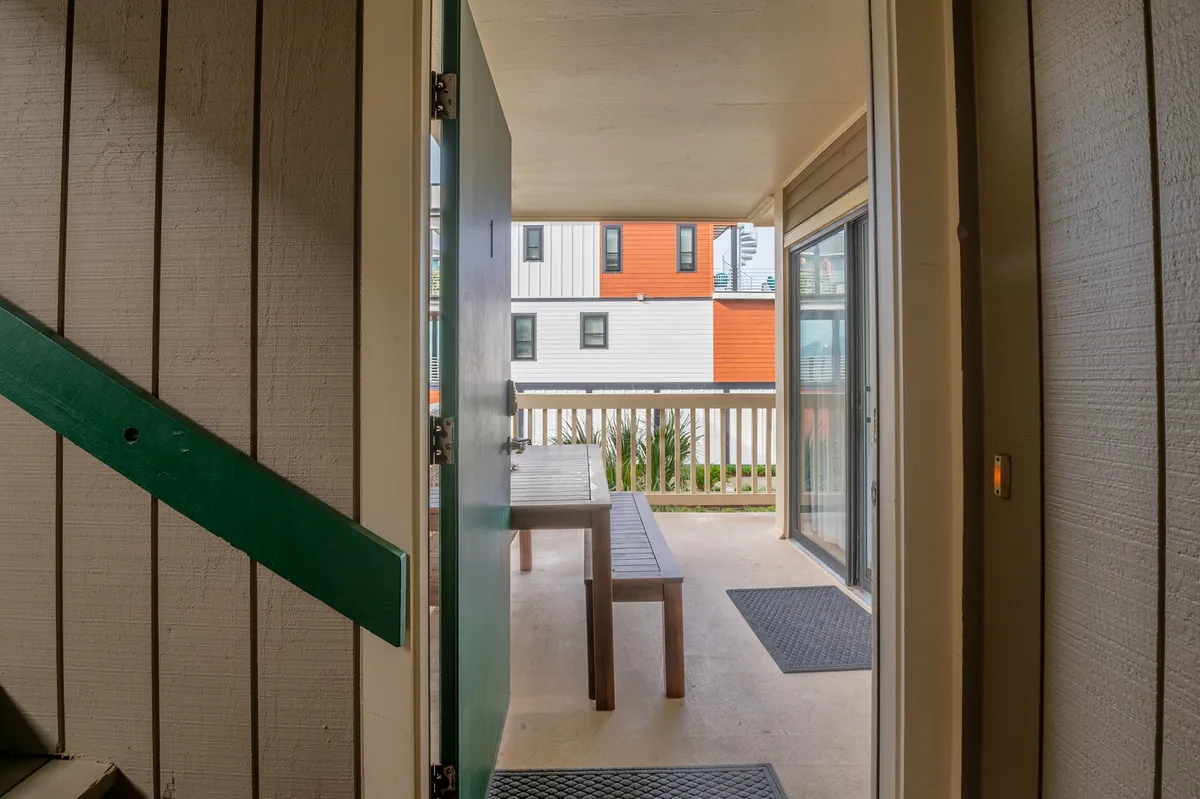 This image shows a green door opening to a small patio area with a wooden bench facing outwards. Beyond the bench, there’s an inviting outdoor view, hinting at the proximity to the ocean and blending indoor comfort with the natural world. The bench suggests a quiet place to enjoy sunrises or unwind after work, while the door connects the private condo to the greater outdoors.