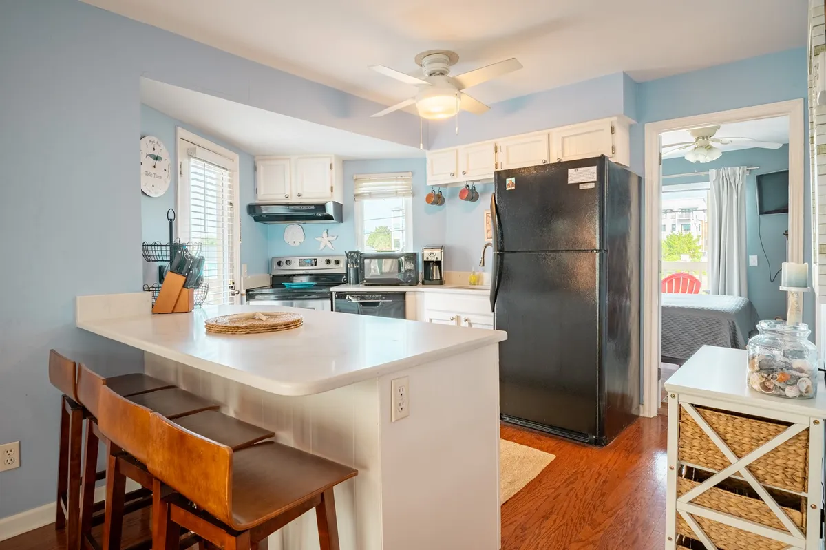 A welcoming kitchen scene featuring a kitchen island, black refrigerator, inviting blue walls, and a window that brings in natural light. The space looks well-equipped and ready for meal preparation or social gatherings.