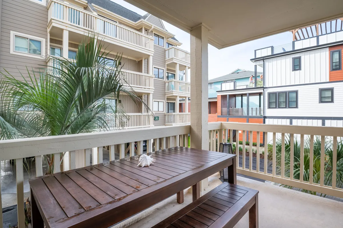 A welcoming dining area with a wooden table surrounded by palm leaves and glimpses of building facades, evoking a sense of warmth and togetherness. The setting suggests meals shared against a backdrop of natural greenery and coastal charm.