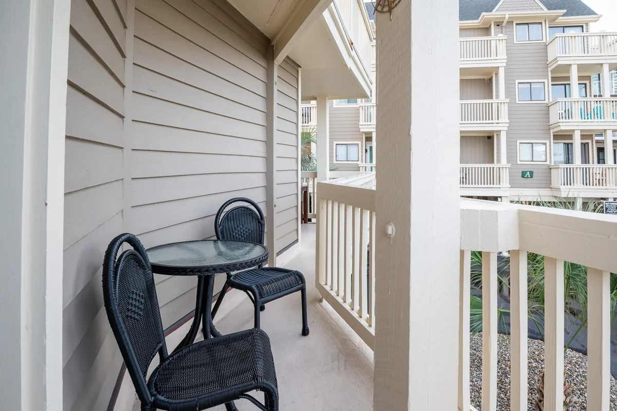 An exterior shot of a private balcony, complete with a bistro table and two chairs set behind a balcony railing. The setup is perfect for morning coffee or evening relaxation, with the ambiance suggesting peaceful moments above the bustle below.