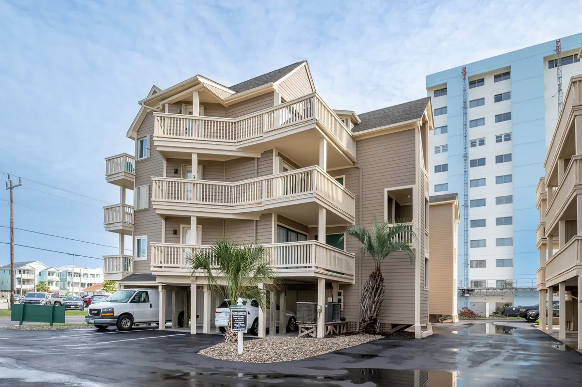 A view of the three-story condominium building, with balconies overlooking palm trees and the parking area below. The setting feels welcoming, with dedicated parking visible and the atmosphere of a secure, relaxed community.