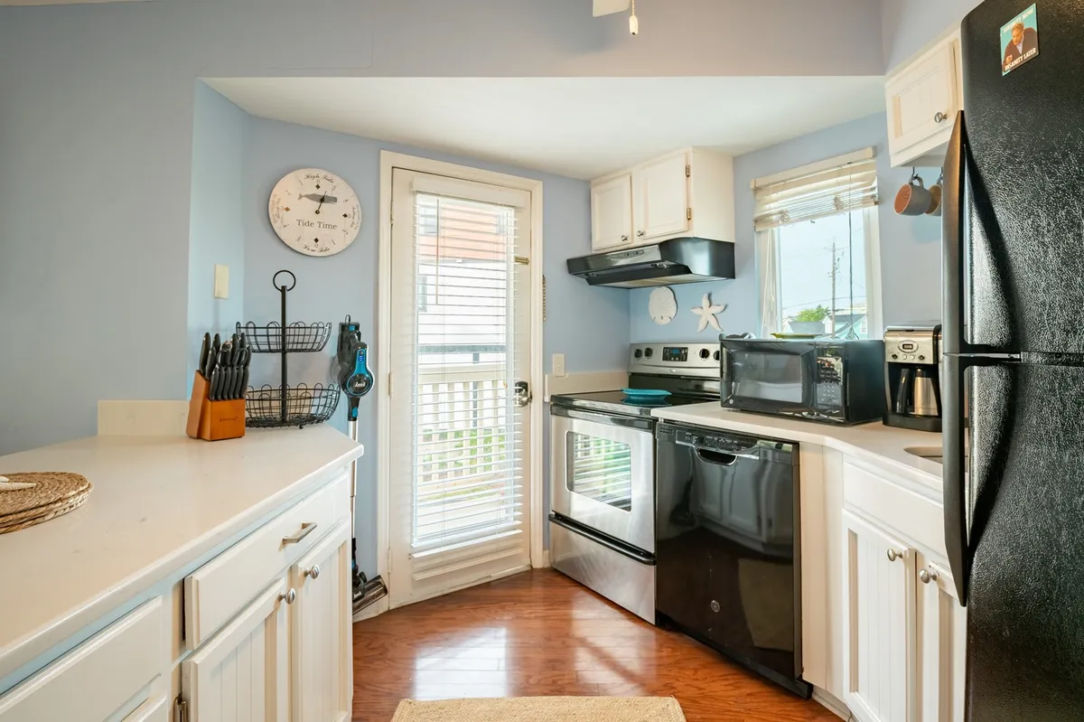 Bright kitchen with white cabinetry, black appliances, a wall clock, and a kitchen window. The space feels cheerful and practical, ideal for cooking or savoring a cup of coffee while enjoying the view.