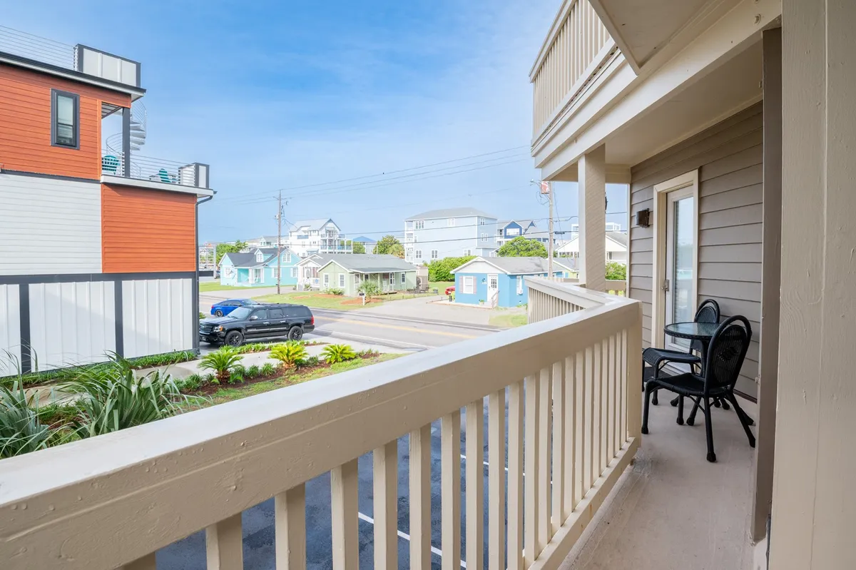 An exterior view from a balcony features stylish outdoor furniture and a view toward the lively yet peaceful street below. The balcony is bathed in natural light, suggesting plenty of opportunities for people-watching, relaxing, and soaking in the local vibe.